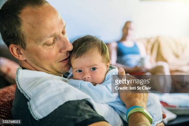 caucasian father burping baby boy in living room - burping stock-fotos und bilder
