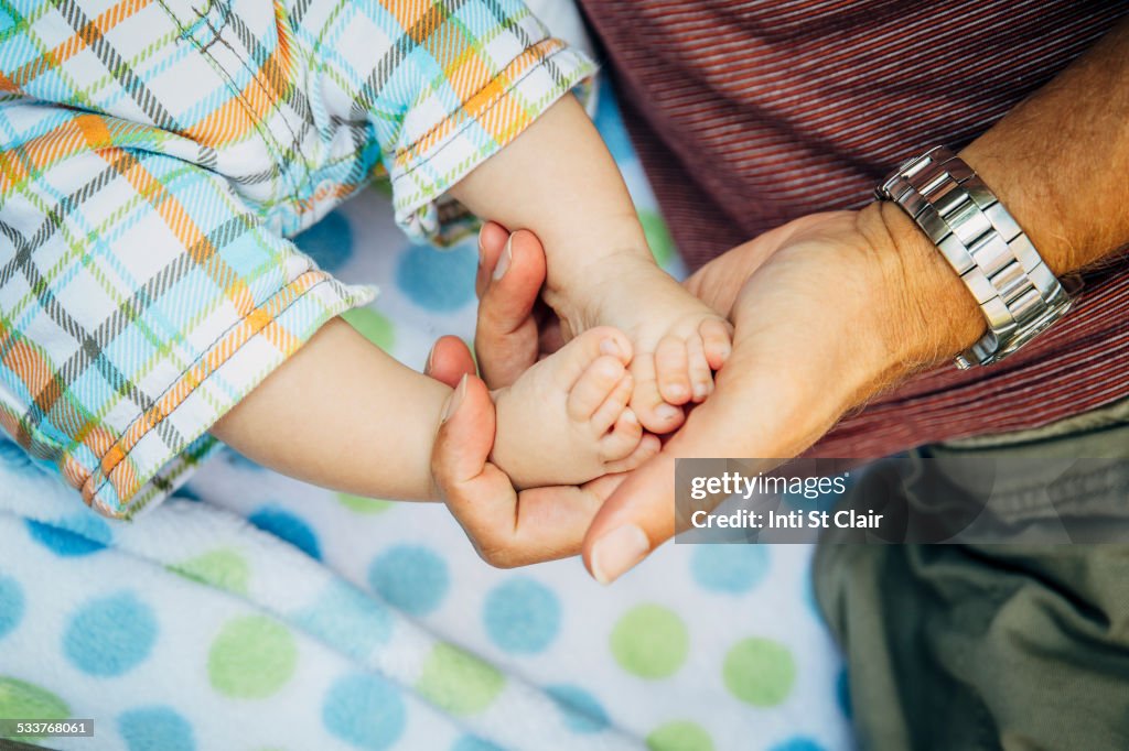 Close up of Caucasian father holding feet of baby boy