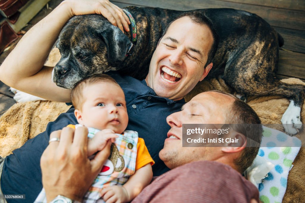 Caucasian gay couple cuddling baby boy and dog