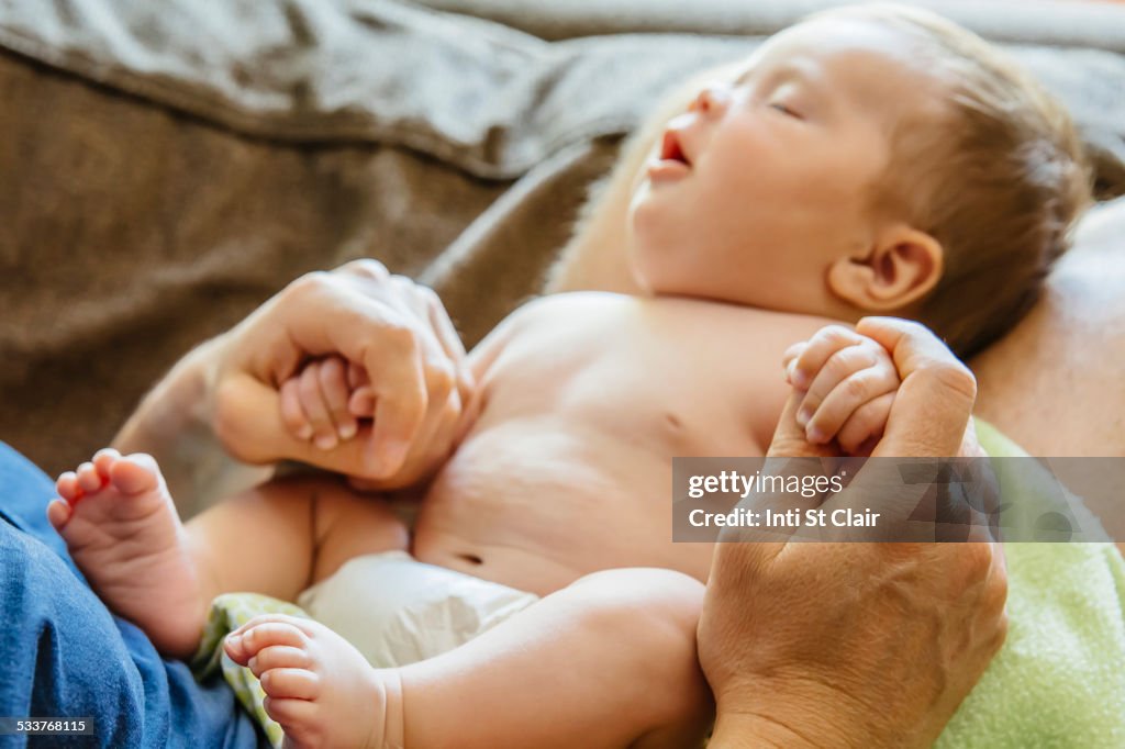 Caucasian father holding sleeping baby boy on sofa