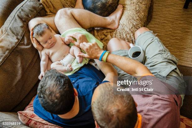 Caucasian gay couple holding sleeping baby boy on sofa