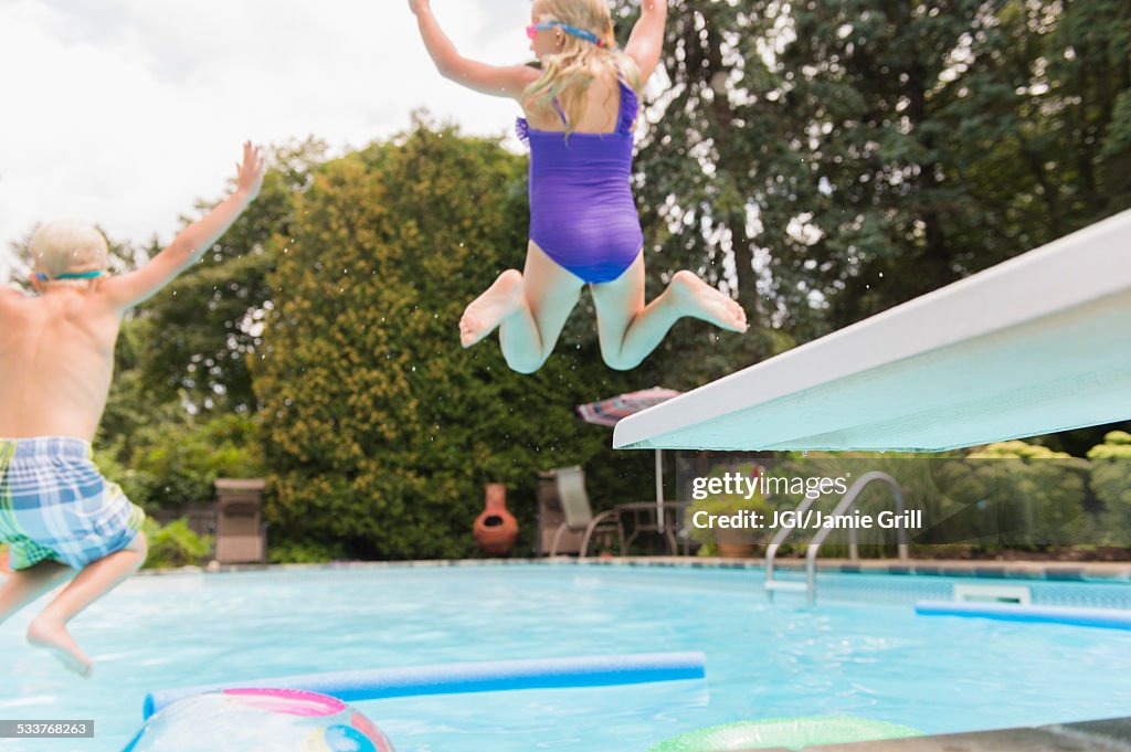 Caucasian children jumping into swimming pool