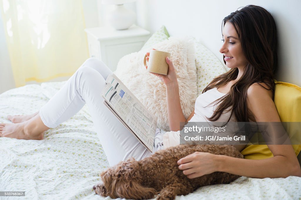 Caucasian woman reading magazine with pet dog in bed