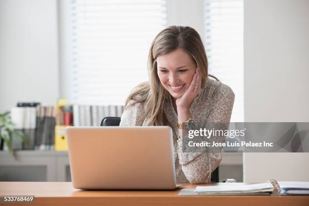 caucasian businesswoman using laptop in office - young blonde woman facing away photos et images de collection