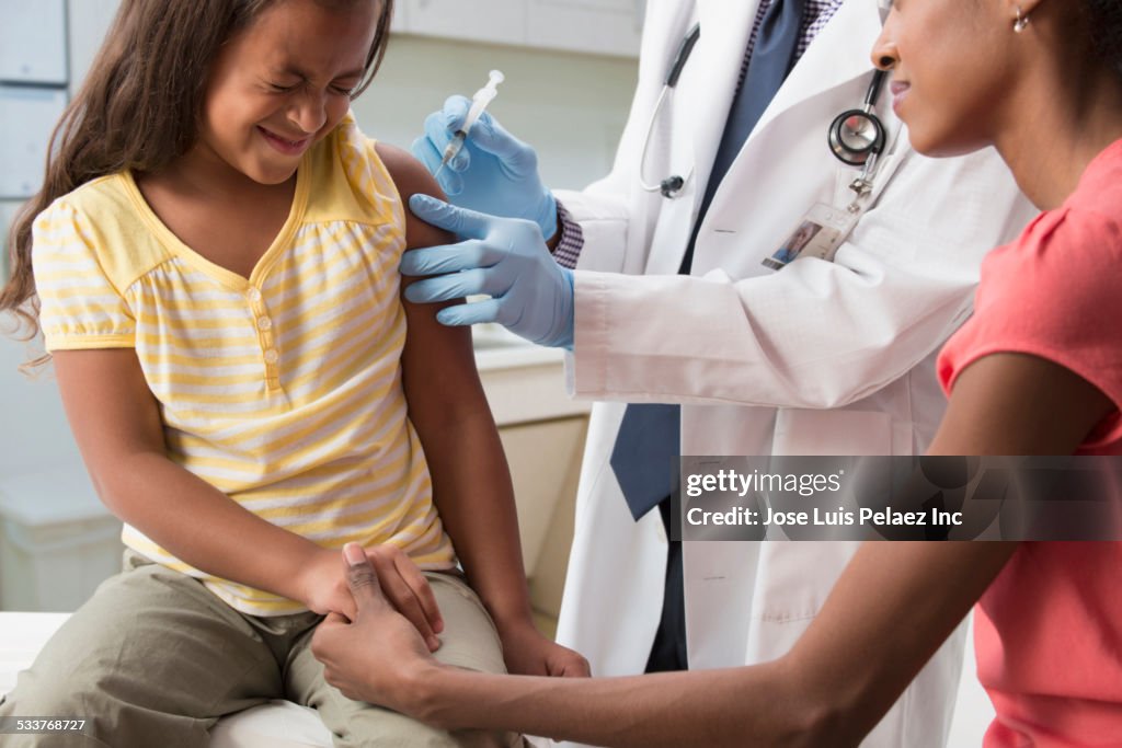 Mother comforting daughter with doctor injecting vaccine