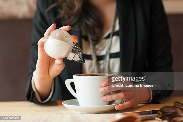woman sprinkling sugar in coffee in cafe - zucker stock-fotos und bilder