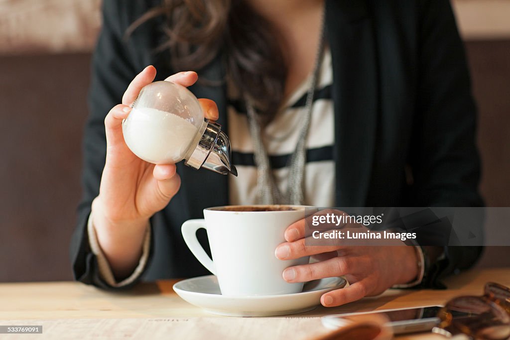 Woman sprinkling sugar in coffee in cafe