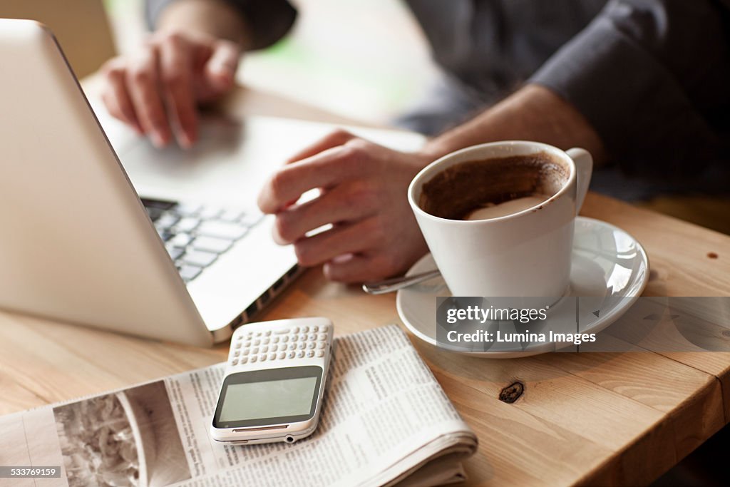 Close up of man using laptop with cup of coffee in cafe