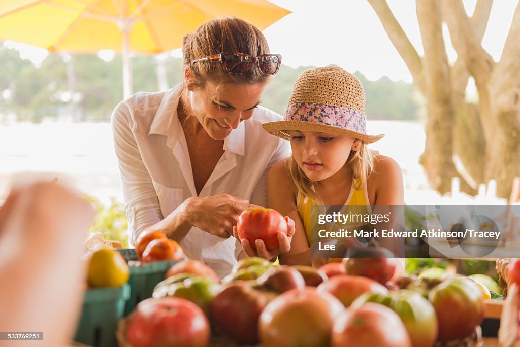 Mixed race mother and daughter browsing produce at farmers market