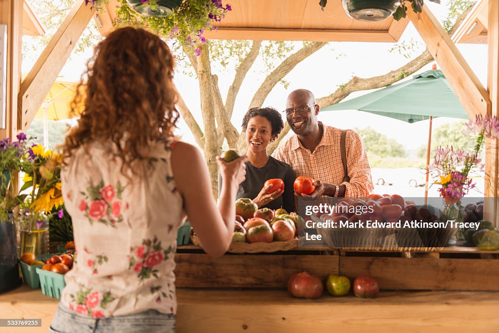 Vendor showing produce to couple at farmers market