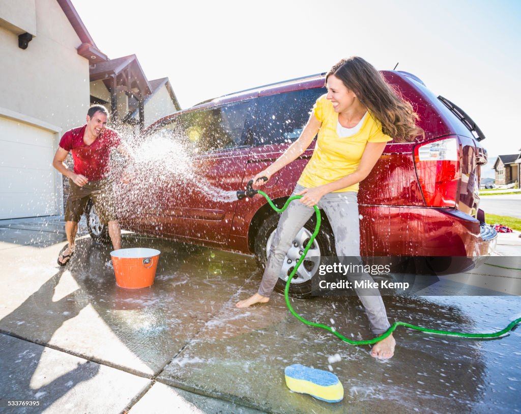 Caucasian couple playing while washing car in driveway