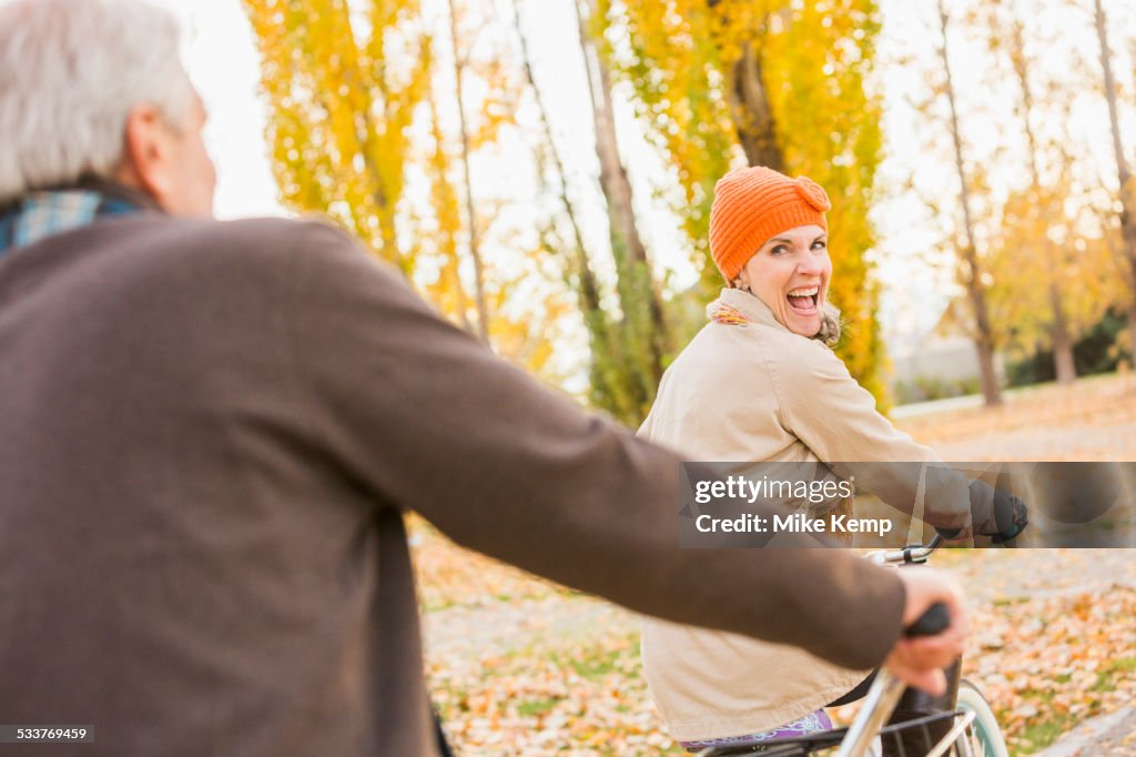 Older Caucasian couple riding bicycles on autumn leaves