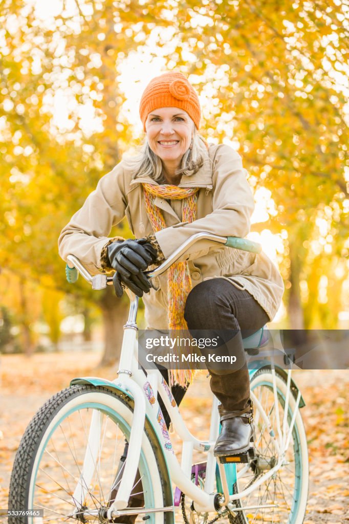 Older Caucasian woman riding bicycle on autumn leaves