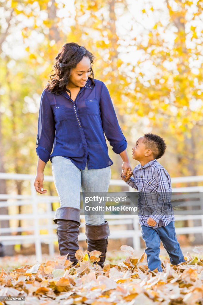 Black mother and son holding hands in autumn leaves