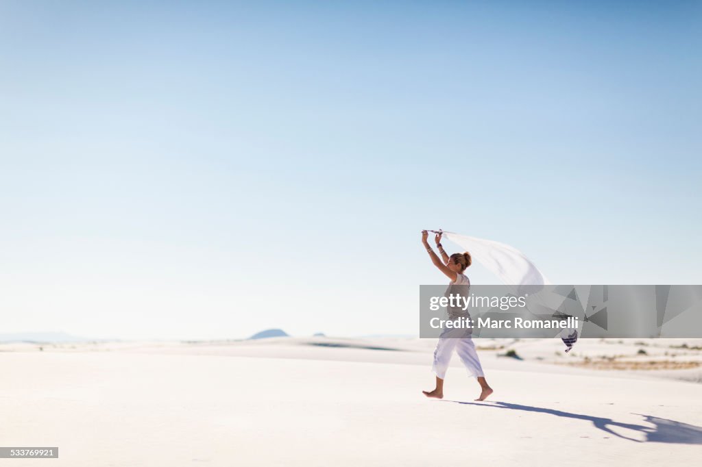 Caucasian woman playing with scarf on sand dune