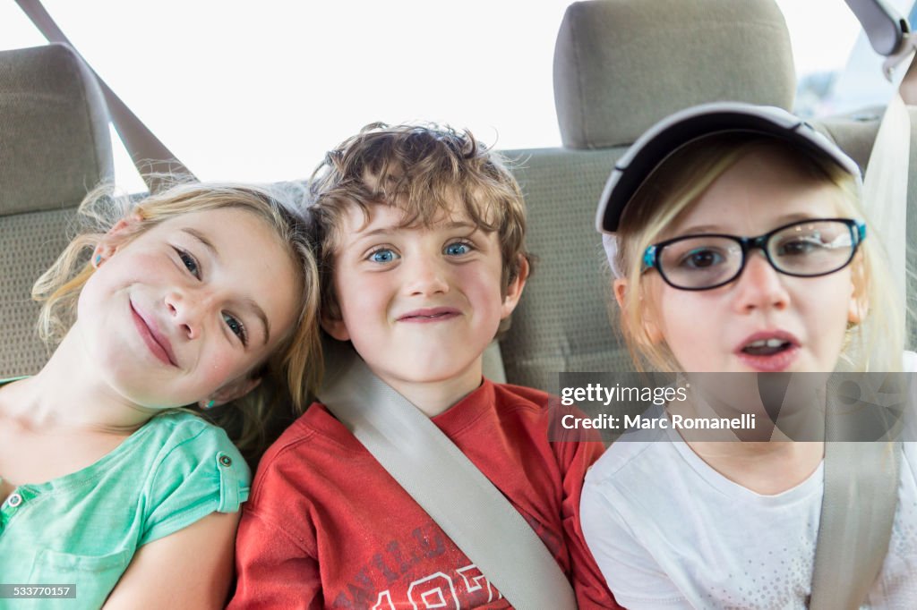 Caucasian children smiling in back seat of car