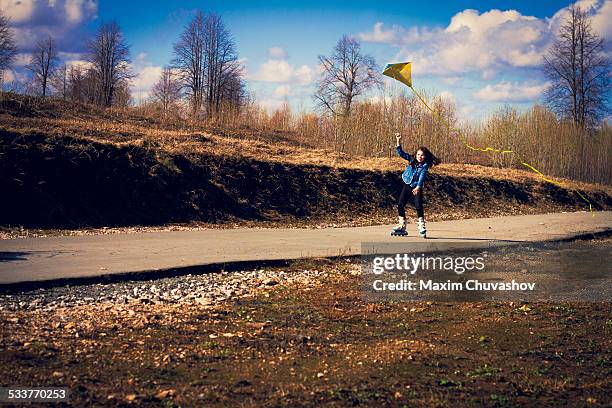 caucasian girl on inline skates flying kite on rural road - inline skating - fotografias e filmes do acervo