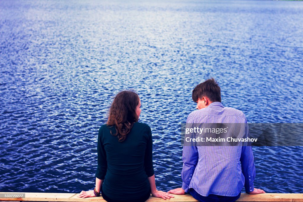 Caucasian couple sitting on dock at lake