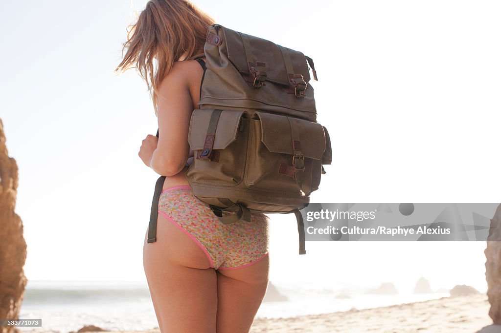 Rear view of mid adult woman wearing backpack and lace knickers on El Matador Beach, Malibu, California, USA
