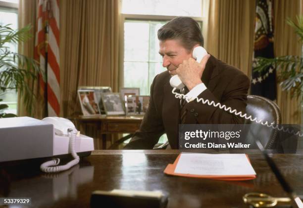 President Ronald Reagan talking on the telephone to the astronauts on space shuttle Columbia's third mission while sitting in the Oval Office of the...