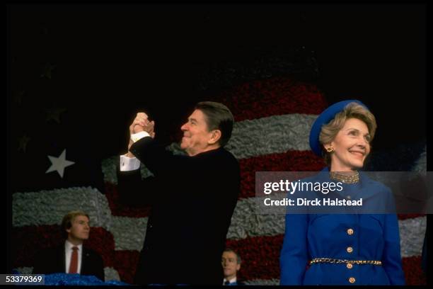 President Ronald Reagan holding up arms victoriously as wife Nancy looks on at post-inaugural gathering of marching bands at the Capitol Center.