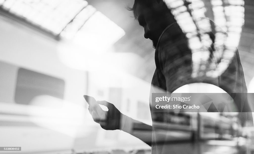 Double exposure of man using phone and train station
