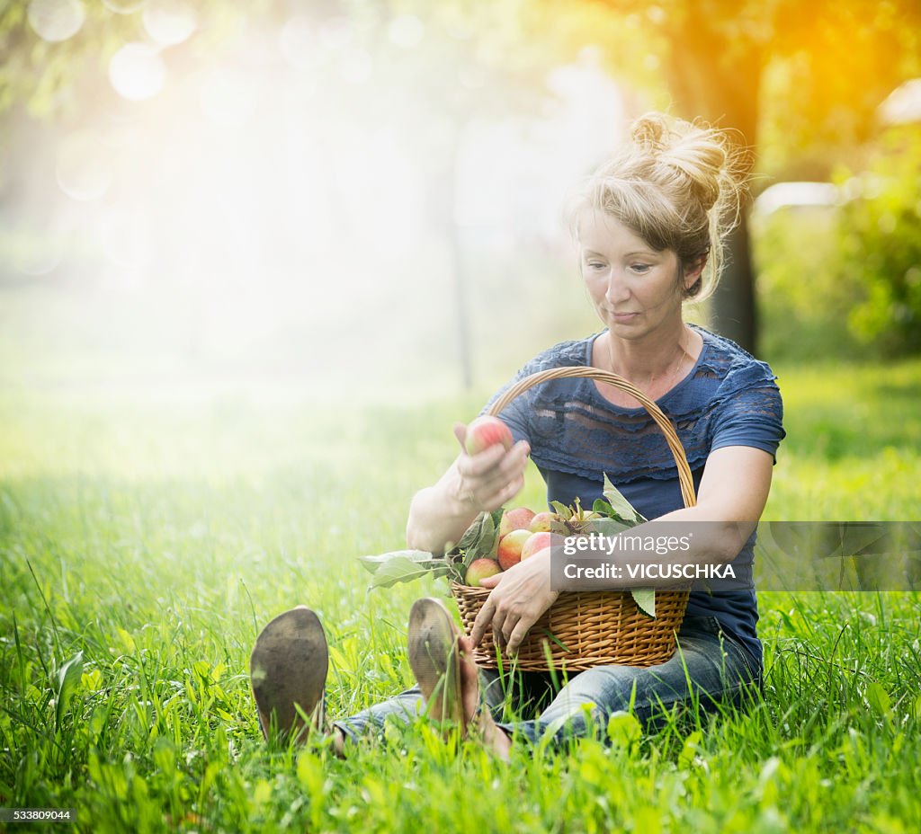 Woman on the grass with basket of apples on her lap
