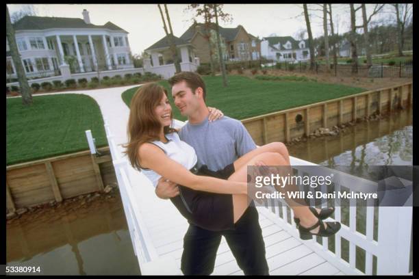 Race car Driver Jeff Gordon carrying wife Brooke on a dock in the backyard of their home.