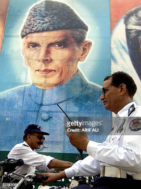 Two Pakistani policemen guard a street standing in front of a portrait of the country's founder Mohammad Ali Jinnah in Lahore, 13 August 2005, a day...