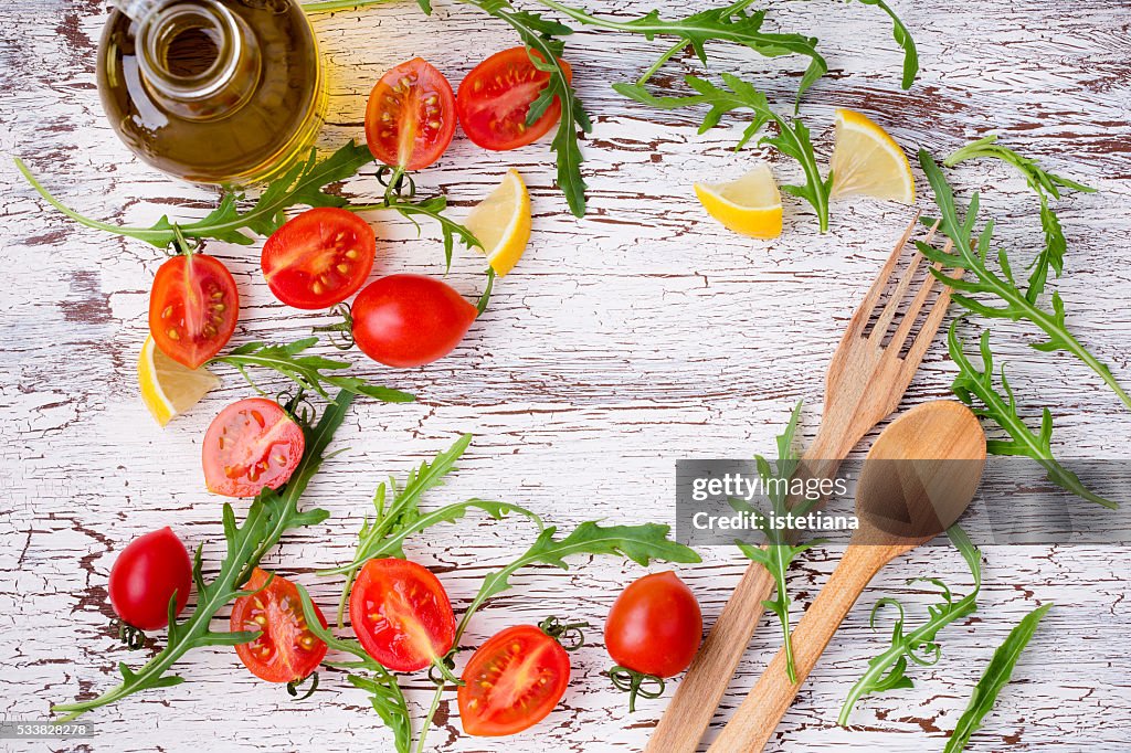 Frame of fresh raw salad ingredients and wooden spoon and fork on rustic wooden   table with central copy space, overhead view