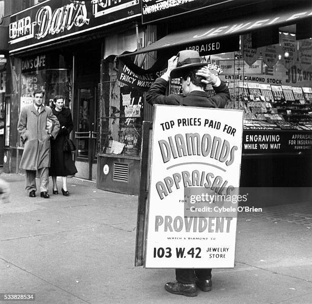 Man carrying a sandwich board scratches his head in front of the diamond store for which he advertises.