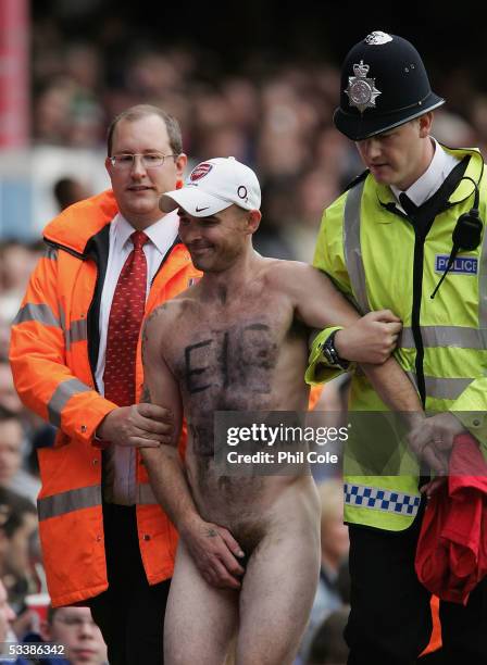 Streaker is escorted off the pitch during the Barclays Premiership match between Arsenal and Newcastle United at Highbury on August 14, 2005 in...