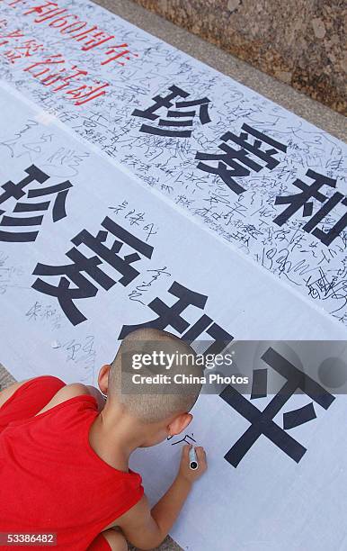 Chinese young boy signs his name on a banner reading" Cherish Peace" during a signature activity to mark 60th anniversary of China's victory in the...