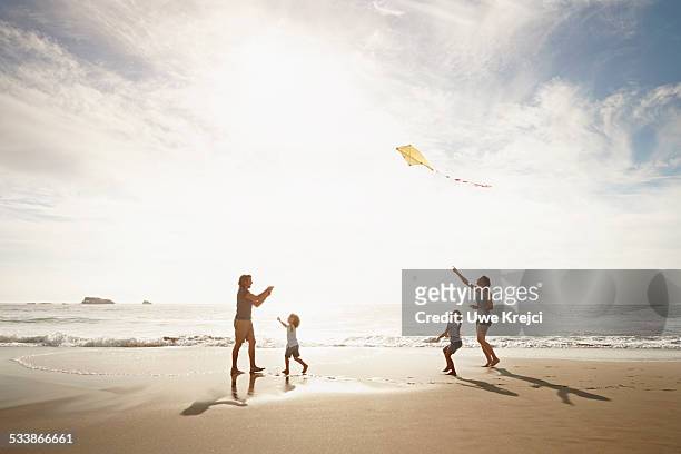 family playing with kite on beach - bright white people stock pictures, royalty-free photos & images