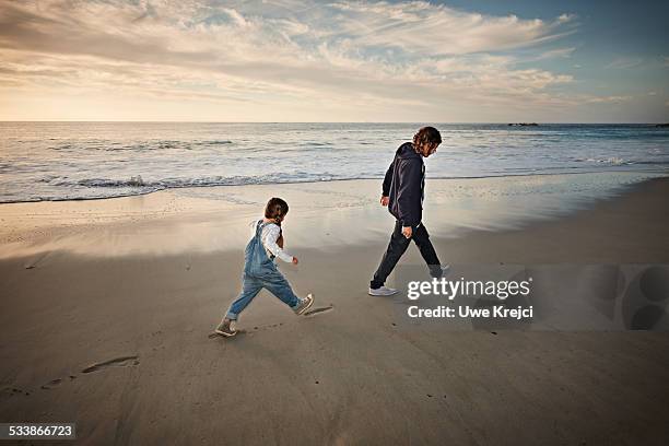 father and daughter walking on beach - voetstappen stockfoto's en -beelden