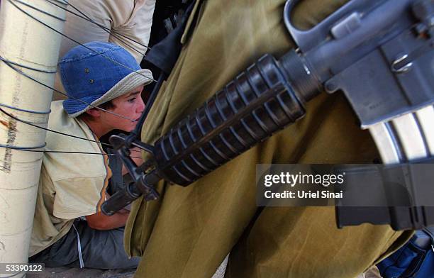 An opponent of the disengagement plan is seen behind an Israeli soldier as she sits behind the fence, August 15, 2005 in the Israeli settlement of...