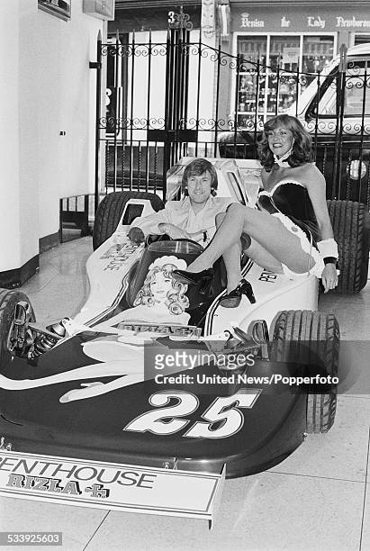 English racing driver Guy Edwards pictured sitting in the driver's seat of the Hesketh 308D car in Penthouse Rizla Racing livery beside Penthouse Pet...