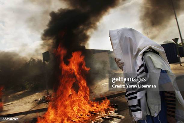 An Israeli settler, covering himself with Talit, passes by a fire on the streets during the evacuation of the settlement of Neve-Dekalim on August...