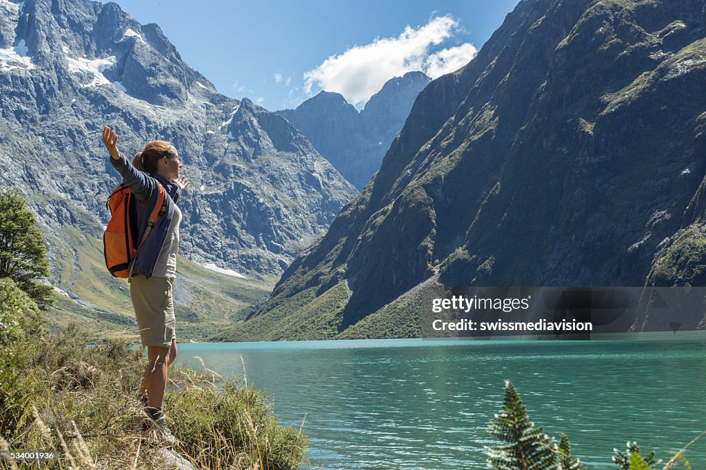 Cheerful young woman hiking reaches the lake Marian, arms outstretched
