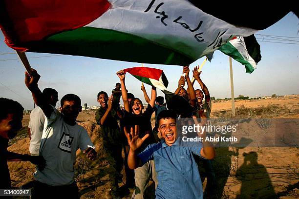 Palestinian boys wave Palestinian flags and cheer near the settlement of Morag August 17, 2005 at their post in Rafah refugee camp in the southern...