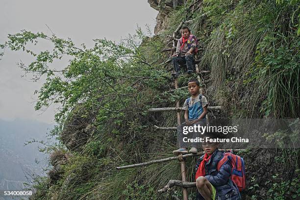 Children of Atule'er Village take a rest during climbing the vine ladder on a cliff on their way home in Zhaojue county in southwest China's Sichuan...