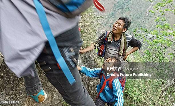Man watches children of Atule'er Village climbing a cliff on their way home in Zhaojue county in southwest China's Sichuan province on May 14, 2016...