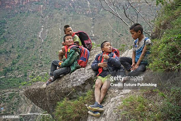 Children of Atule'er Village take a rest during climbing the cliff on their way home in Zhaojue county on May 14, 2016 in Zhaojue, China. There are...