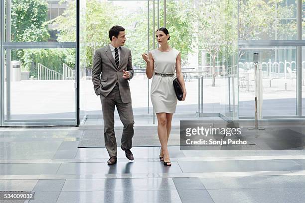 business man and business woman walking in office lobby - abbigliamento elegante foto e immagini stock