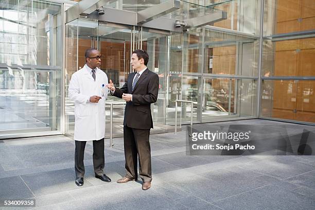 business man and doctor talking outside office building - medical protective suit stock pictures, royalty-free photos & images