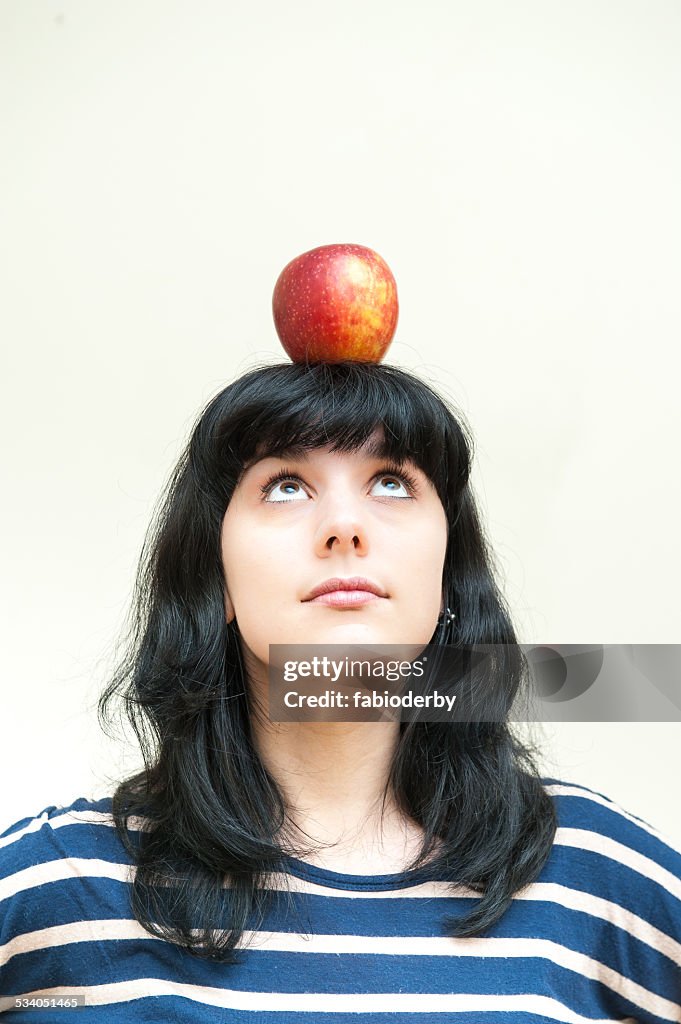 Pretty brunette girl looking red apple on head