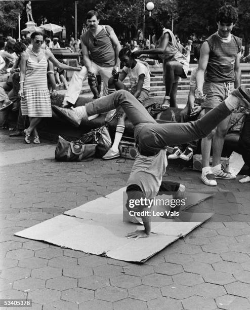 Watched by a group of spectators, a young man breakdances in Washington Square Park, New York, New York, early 1980s.