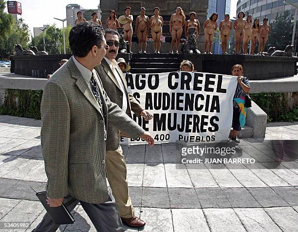 Two men pass in front of peasant women, members of the "Los 400 Pueblos " group, who demonstrate in the nude in Mexico City, 18 August 2005,...