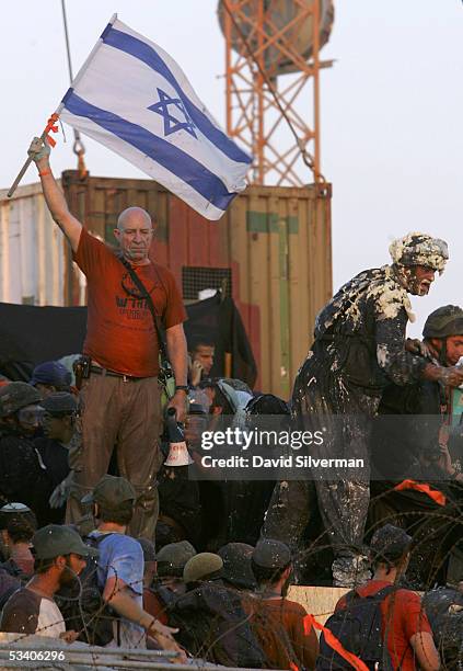 Right-wing Israeli activist leader Colonel Moshe Leshem waves the Israeli flag as Israeli riot police break onto the synagogue roof where hundreds of...