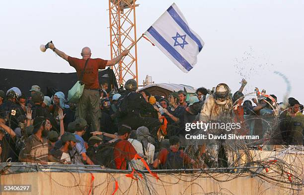 Right-wing Israeli activist leader Colonel Moshe Leshem waves the Israeli flag as Israeli riot police break onto the synagogue roof where hundreds of...